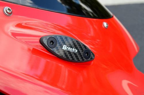 Brock's Performance Brocks Carbon Fiber Mirror Block Off Plates Kawasaki ZX14R (06-25), close-up of black carbon fiber mirror block off plate mounted on a red motorcycle body with bolts. Brock's Performance Brocks Carbon Fiber Mirror Block Off Plates Kawasaki ZX14R (06-25), close-up of black carbon fiber mirror block off plate mounted on a red motorcycle body with bolts.