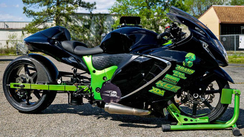 Baxley Drag Chock, a green and black motorcycle wheel chock with safety labels and a wheel lock, used for securely holding racing bikes on trailers or stands.