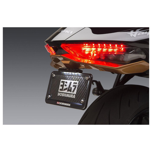 Yoshimura Fender Eliminator Kit Suzuki Hayabusa (22-25), close-up view of the black carbon fiber license plate holder with Yoshimura logo, installed on the rear of a black Suzuki Hayabusa motorcycle with illuminated tail lights. Loading Image