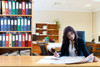 woman reads newspaper amidst shelves of colorful binders