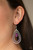 A purple teardrop bead is nestled inside two silver teardrops radiating in studded textures, creating a dizzying lure. Earring attaches to a standard fishhook fitting.

Sold as one pair of earrings.