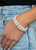 Held in place with white rhinestone encrusted silver fittings, pairs of pearly white beads are threaded along stretchy bands around the wrist.

Sold as one individual bracelet.