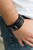 A collection of leather pieces and antiqued gunmetal frames are studded in place across the front of a thick leather band, creating an abstract buckle. Features an adjustable snap closure.

Sold as one individual bracelet.
