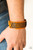 Shiny black thread is stitched across the front of a brown leather band. The crisscrossing threads create a tactile pattern around the wrist. Features an adjustable buckle closure.

Sold as one individual bracelet.