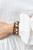A mismatched collection of brown wooden beads, silver accents, cat eye stones, and glassy orange beads are threaded along stretchy bands, creating colorful layers around the wrist.

Sold as one set of three bracelets.
