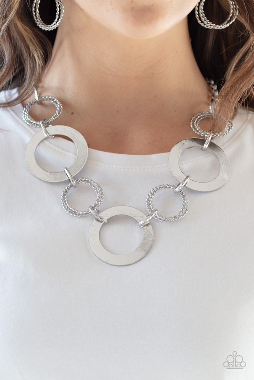 Flat silver circles link with trios of twisted silver rings below the collar for a dramatic industrial display. Features an adjustable clasp closure.

Sold as one individual necklace. Includes one pair of matching earrings.