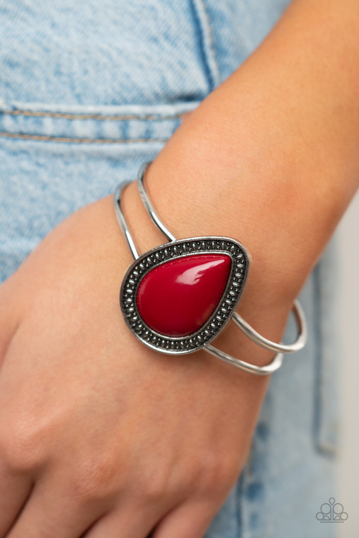 A shiny red teardrop bead is pressed into the center of a studded silver frame atop an airy silver cuff, creating a vibrant pop of color around the wrist. Features a hinged closure.

Sold as one individual bracelet.