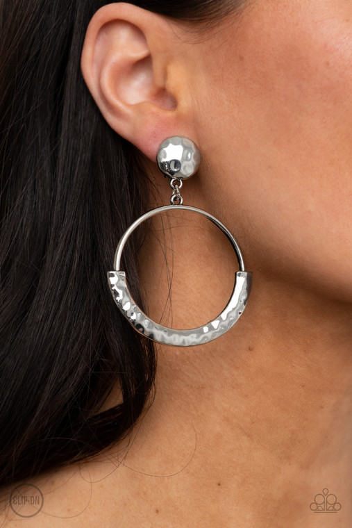 The bottom of an antiqued silver hoop is covered with a bowing hammered frame at the bottom of a hammered silver disc, creating a rustic lure. Earring attaches to a standard clip-on fitting.

Sold as one pair of clip-on earrings.