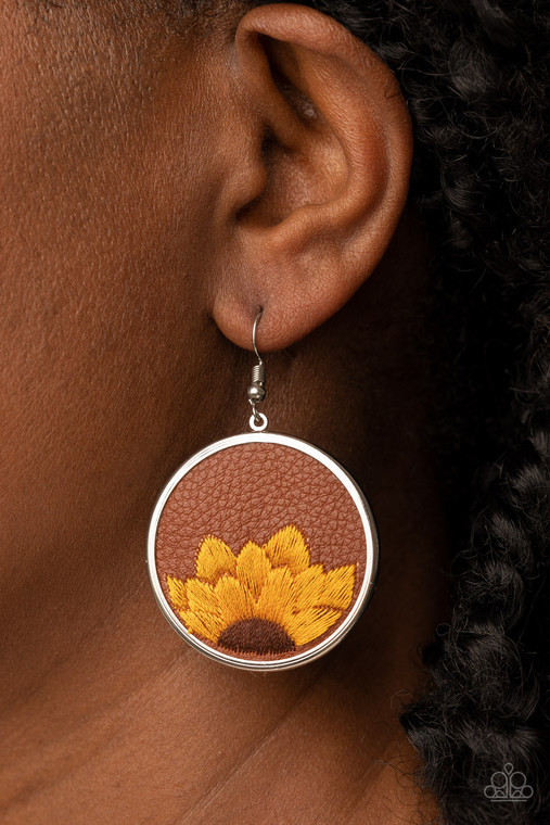 A golden yellow and brown threaded sunflower is stitched into the bottom of a brown leather frame that is encased in a sleek silver frame, resulting in a whimsical floral fashion. Earring attaches to a standard fishhook fitting.

Sold as one pair of earrings.