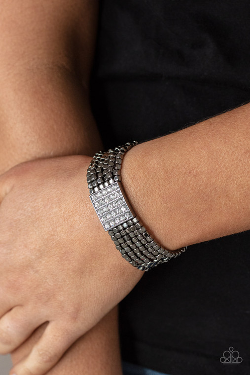 Held in place by a square centerpiece encrusted in row after row of dazzling white rhinestones, a dainty collection of gunmetal cube beads are threaded along stretchy bands around the wrist, creating shimmery layers.

Sold as one individual bracelet.