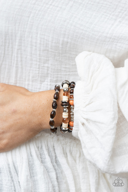 A mismatched collection of brown wooden beads, silver accents, cat eye stones, and glassy orange beads are threaded along stretchy bands, creating colorful layers around the wrist.

Sold as one set of three bracelets.