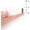 Green capsule on a fingertip beside a ruler for size