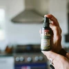 Hand holding Olive Leaf Complex Throat Spray in a kitchen