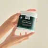 Hand holding open maca powder jar showing beige powder