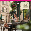 Woman smiling on phone at outdoor cafe, Bach lifestyle graphic