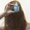 Woman with reddish-brown hair holding Scalp Care Density Serum bottle