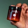 Hand holding a FODZYME enzyme powder jar on a green background
