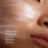 Cream on a woman's cheek, fine lines and firmness callout