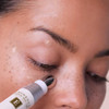 Hand applying Vitamin C+ Eye Cream with metal rollerball under eye