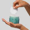 Hand lifting a toner pad from an open HydroPeptide jar