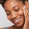 Smiling model applying serum to cheek