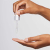 Hand holding a dropper of AGE Bright Clearing Serum above an open palm