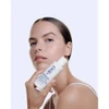 Woman holding Obagi CLENZIderm cleanser bottle to her face