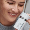 Smiling woman holding PowerBright Overnight Cream near her face