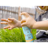 Child's hands near a Babo Botanicals SPF 30 spray bottle outdoors