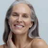 Smiling gray-haired woman touching her neck