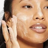 Woman massaging creamy exfoliant onto her cheeks