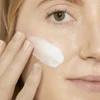 Woman applying white sunscreen to her cheek