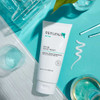Replenix BP 5% Acne Wash tube on teal with a swatch and glassware