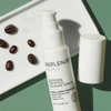 Uncapped serum bottle with coffee beans on a green surface