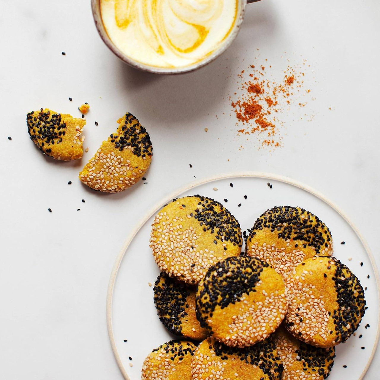 Golden milk in a cup beside sesame-coated cookies on a plate
