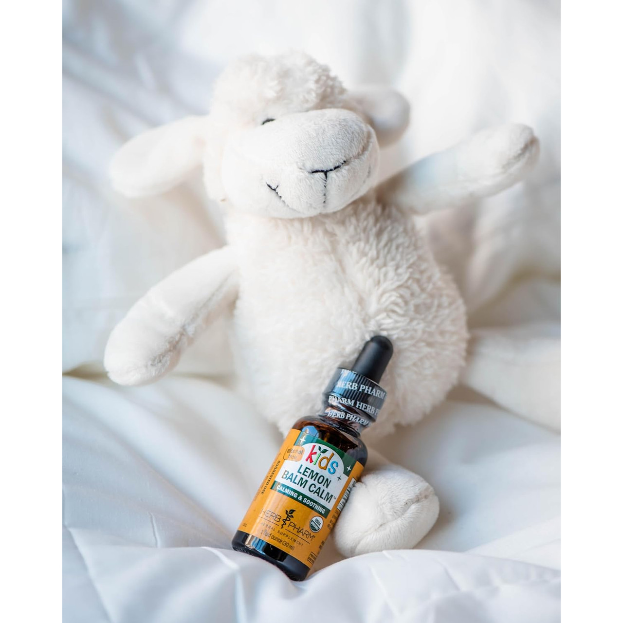 Kids Lemon Balm Calm bottle beside a white plush sheep on a bed
