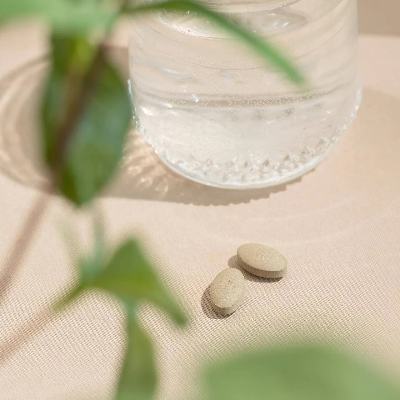 Two tablets beside a glass of water and green leaves