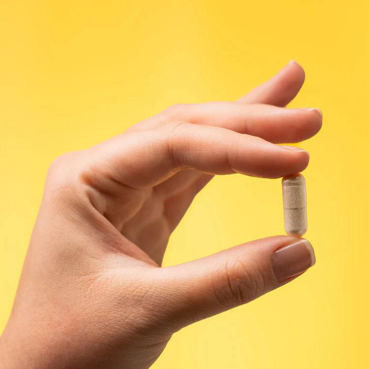 Fingers holding a single capsule on a yellow background