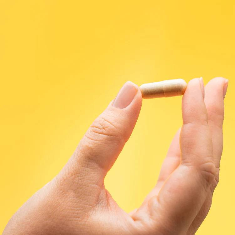Hand holding a beige capsule against yellow background