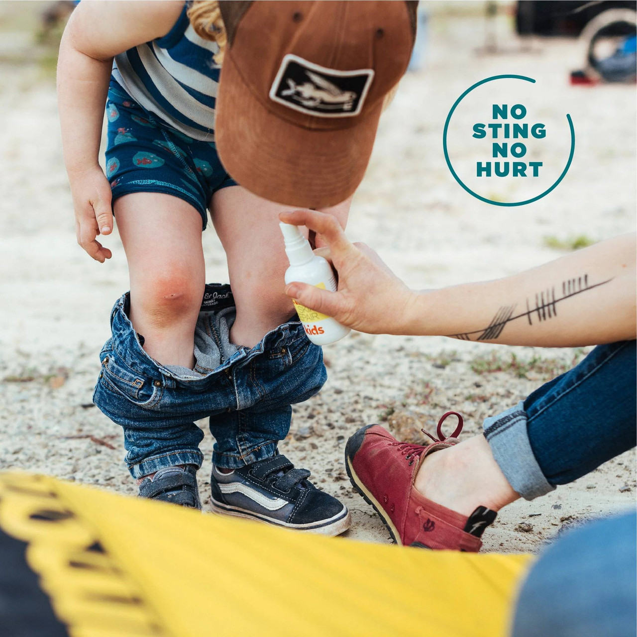 Parent treating a child's knee outdoors, no sting no hurt graphic