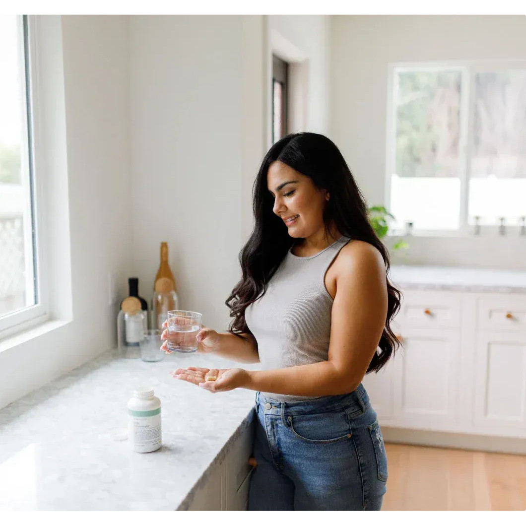 Woman in a kitchen holding a glass of water and capsules