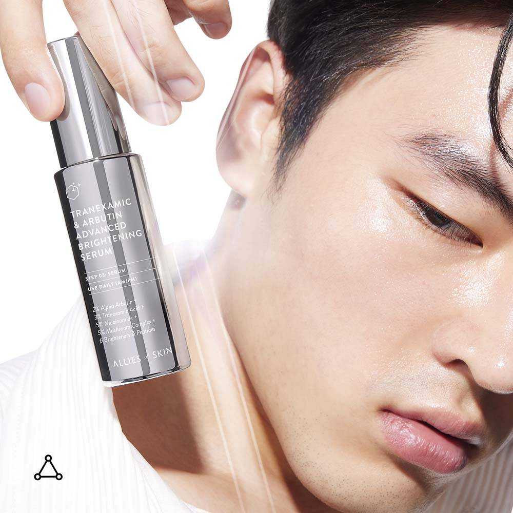 Man holding the Tranexamic & Arbutin serum bottle near his face
