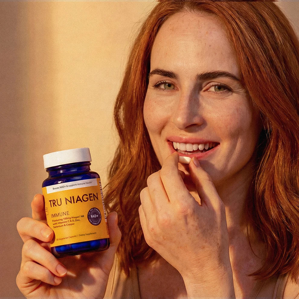 Woman taking a capsule holding a Tru Niagen Immune bottle