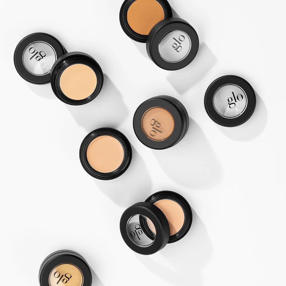 Several open concealer compacts scattered on a white surface