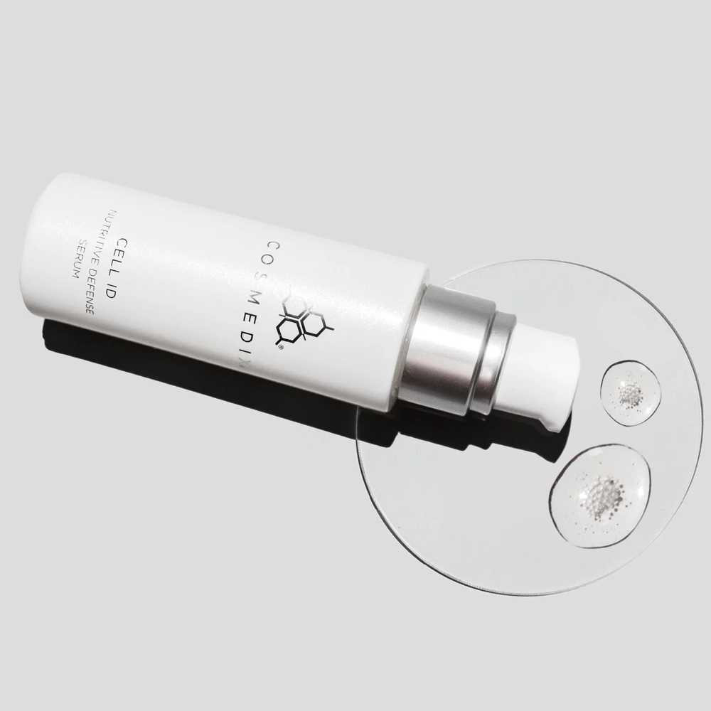 CosMedix serum bottle on its side beside a glass dish with serum drops