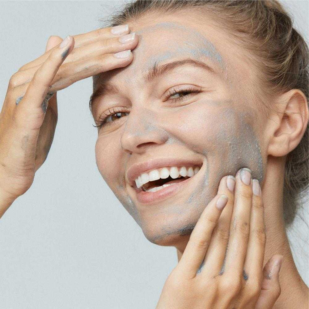 Smiling woman with gray Daily Superfoliant paste on her face