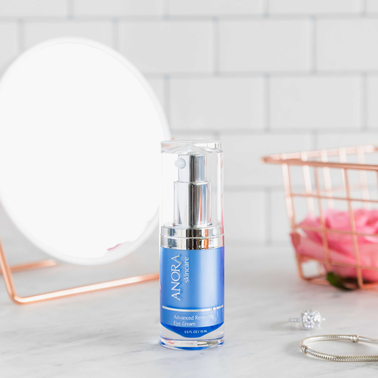 Anora Eye Cream on a counter beside a round mirror and pink roses