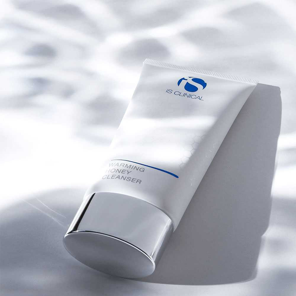 iS Clinical Warming Honey Cleanser tube leaning on a gray block