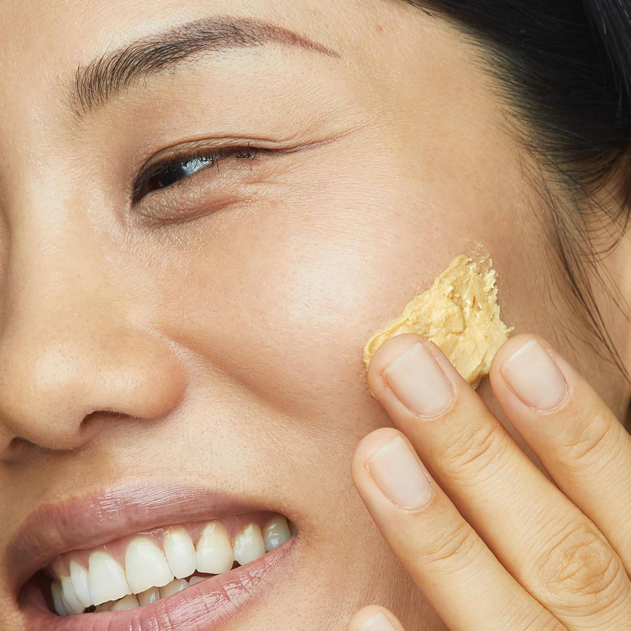 Smiling woman applying yellow scrub to her cheek