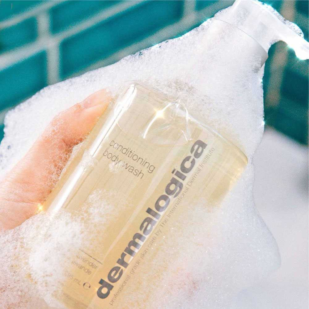 Hand holding a Dermalogica body wash bottle covered in foam